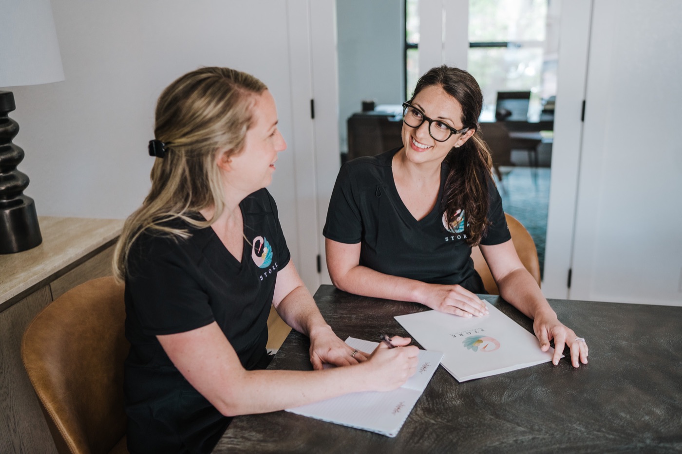Katie and Leah meeting with a family while wearing Stork scrubs.